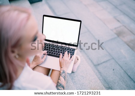Blurred female IT professional with tattooed hand holding mockup laptop with copy space area for internet advertising, millennial blogger with blank netbook creating web design for online project