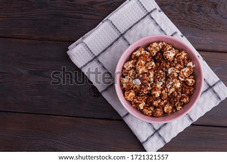 Close up popcorn covered chocolate in pink bowl on dark wooden background. Homemade chocolate popcorn. Concept of watching tv at home.