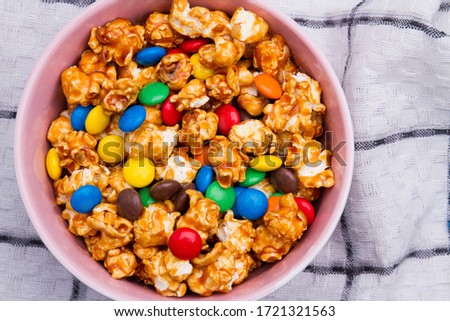 Chocolate candies and golden popcorn mix in ceramic plate on white napkin. Close up picture from top.