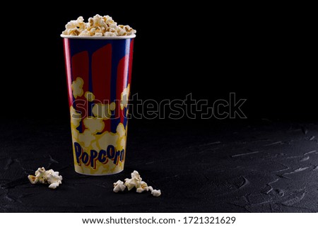 Full popcorn in classic popcorn box on very dark background. Red and blue colors on cartoon box.