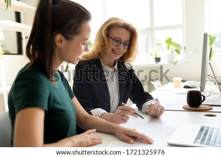Happy young businesswoman presentation project using laptop for mature female mentor in boardroom at meeting. Smiling leader presenting new business concept for woman colleague discuss. Royalty-Free Stock Photo #1721325976