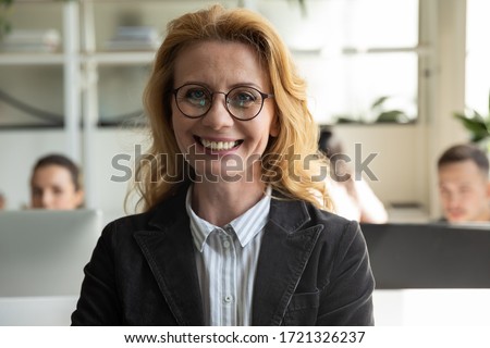Close up headshot portrait picture of happy attractive mature businesswoman with glasses. Smiling confident middle age woman manager looking at camera on workplace background in office.