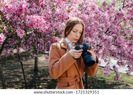 A young beautiful girl photographer walks and takes photos on against a blooming Apple tree. Hobbies, recreation