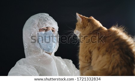 Ginger cat paw vet in the face. Male virologist in a protective suit and medical mask holds a wild cat in his hands. Rabies in pets. Royalty-Free Stock Photo #1721332834