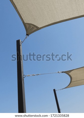 Three ends of white sun-protection cover attached to the two poles under bright blue sky