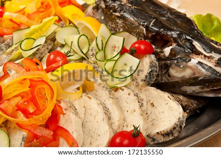 Stuffed sliced pike with head, decorated with tomato, lemon and cucumber close up in restaurant