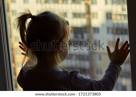Girl looks lonely through window by putting her hands on window sill