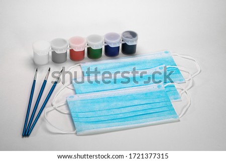 Blue medical masks lie on a white background together with paints for painting and brushes. Hobbies during self-isolation.