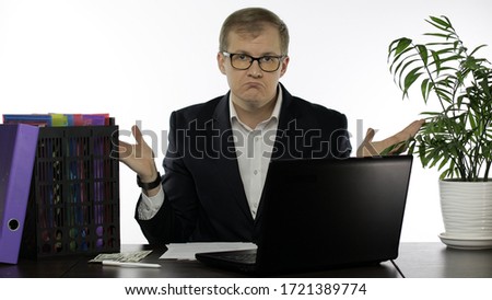 Shocked young businessman manager sitting at office shrugging shoulders in hesitation doubting. Office people. Problems. Emotions. Guy in suit, shirt, glasses. White background