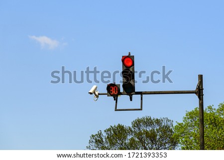 Red traffic light with digital timing countdown and traffic security camera surveillance (CCTV) installed on a pole above a roadway on a sunny day. Modern automatic traffic control. Royalty-Free Stock Photo #1721393353