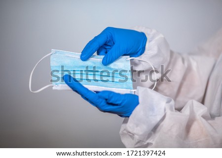 COVID-19. Facial masks on the pile. Epidemic background. Close-up. A medical worker in a protective anti-plague suit holds a maditsin mask with rubber disposable gloves