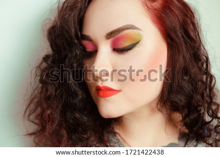 Photo of a girl portrait of a brunette with color makeup, shades of red, green, yellow. Gorgeous professional bright makeup. Girl with a tunnel in the ear. Gorgeous make-up model.