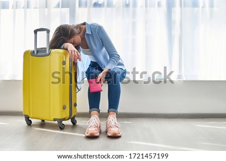 Woman traveler with yellow suitcase affected by flight delay and cancelled travel and vacation holiday. Travel ban and traveling problems  Royalty-Free Stock Photo #1721457199