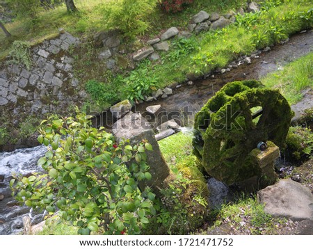 Rural scene with Old green fairy tail watermill wheel overgrown with moss, river flows in background, nature of Kyushu