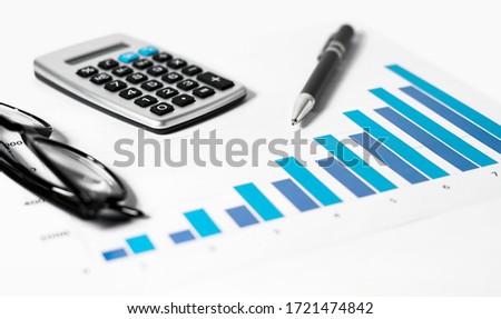 Business accounting analysis report concept with a close up view of a successful growing graph, calculator, pen and glasses on a white desk on background.
