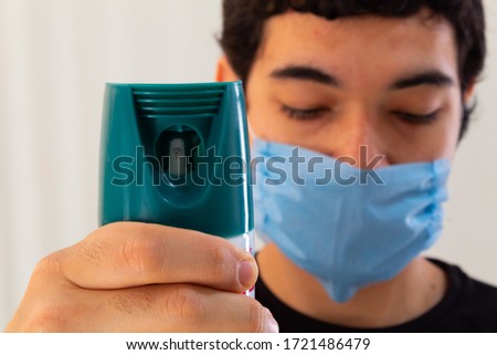 young man wearing a blue medical mask holding a bottle of disinfectant spray