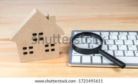 Hand holding a magnifying glass over a home model.
Finding a house. 
Search for housing. 
