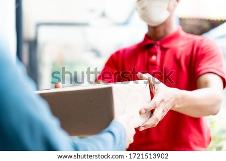 Asian postman, deliveryman wearing mask carry small box deliver to customer in front of door at home. Man wearing mask prevent covid19, corana virus affection outbreak. Home delivery shopping concept. Royalty-Free Stock Photo #1721513902