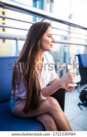 Young woman drinking wine while relaxing on the top at skybar with skyline
