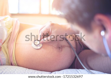 healthcare and medical care concept close up male doctor hand checking up on pregnant woman, using stethoscope checking fetus baby infant inside, pregnancy checkup into parenthood motherhood lifestyle