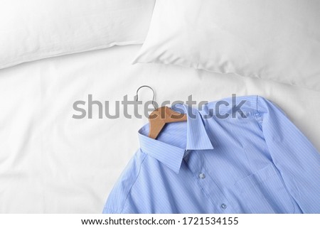 Stylish light blue shirt on bed, space for text. Dry-cleaning service