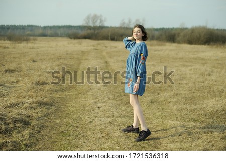 Beautiful teenage brunette girl in dress having fun in the spring field