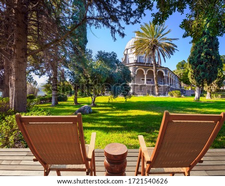 Two comfortable wooden chairs - deck chairs on the platform for relaxing. Catholic Church of the Beatitudes and park around the monastery. The concept of religious pilgrimage and photo tourism