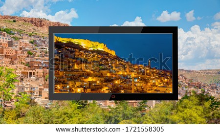 
Flat black TV with picture of sunflowers field on the screen - Day and night concept Mardin old town with bright blue sky - Mardin, Turkey