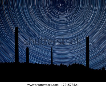 Digital composite image of star trails around Polaris with industrial chimney stacks landscape 