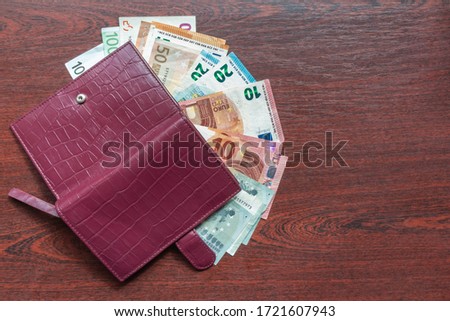 Euro banknotes and leather wallet on wood background. Leather wallet and various kinds of euro notes on desk. Euro banknotes and purple wallet on mahogany table. Purse and salary. Cash payment concept