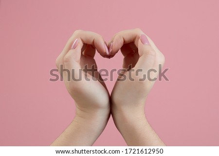 Beautiful womens hands making sign Heart by fingers, isolated on pink background. Female hand showing gesture. Love concept on Valentine day.