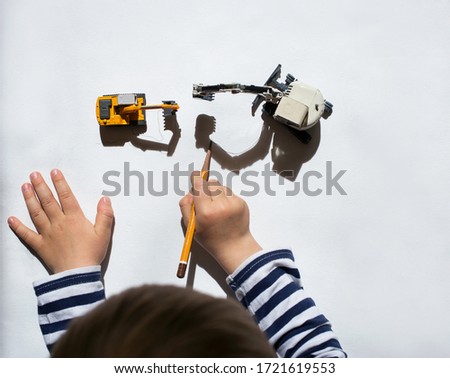 child draws pencil around  contrasting shadows from mini metal models of excavators. drawing of  preschooler, ideas for development of creative thinking. Interesting activities at home for children