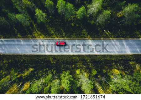 Aerial view of red car on a country road in green forest in Finland