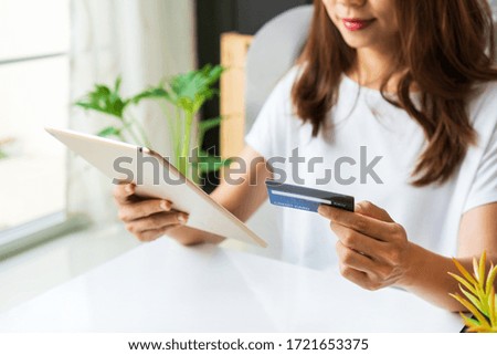 Young Asian woman using tablet while holding credit card in the living room at home, close up