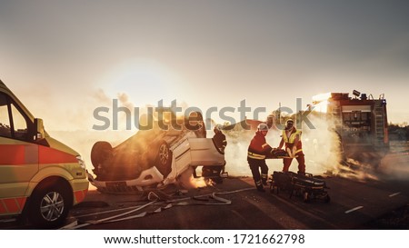 On the Car Crash Traffic Accident Scene: Paramedics and Firefighters Rescue Injured Victim Trapped in the Vehicle. Extricate Person Using Stretchers, Give First Aid and Transport Them to Hospital Royalty-Free Stock Photo #1721662798