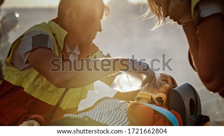 On the Car Crash Traffic Accident Scene: Paramedics Saving Life of a Female Victim who is Lying on Stretchers. They Listen To a Heartbeat, Apply Oxygen Mask and Give First Aid. Royalty-Free Stock Photo #1721662804