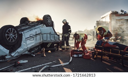 On the Car Crash Traffic Accident: Paramedics and Firefighters Rescue Injured Trapped Victims. Medics give First Aid to Female on Stretchers. Firemen Use Hydraulic Cutters Spreader to Open Vehicle Royalty-Free Stock Photo #1721662813