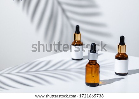 Creative photo of cosmetic bottle with pipette on a white background with shadow of tropical flower. Advertising