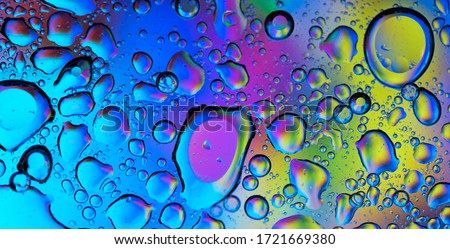 Big and small water and oil drops on a surface that is colored by blue, pink, purple, green and yellow.
