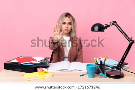 Young student woman working in a table making stop gesture with her hand