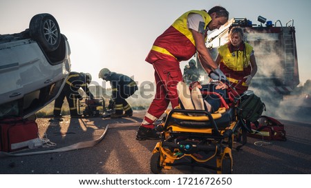On the Car Crash Traffic Accident Scene: Paramedics Saving Life of a Female Victim who is Lying on Stretchers. They Apply Oxygen Mask, Do Cardiopulmonary Resuscitation / CPR and Perform First Aid Royalty-Free Stock Photo #1721672650