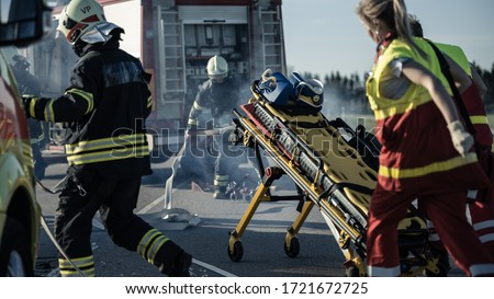 On the Car Crash Traffic Accident Scene: Paramedics and Firefighters Rescue Injured Victims Trapped in the Vehicle. Medics Use Stretchers, Perform First Aid. Firemen Grab Equipment from Fire Engine Royalty-Free Stock Photo #1721672725