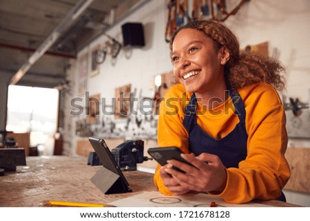Female Business Owner In Workshop Using Digital Tablet And Holding Mobile Phone Royalty-Free Stock Photo #1721678128
