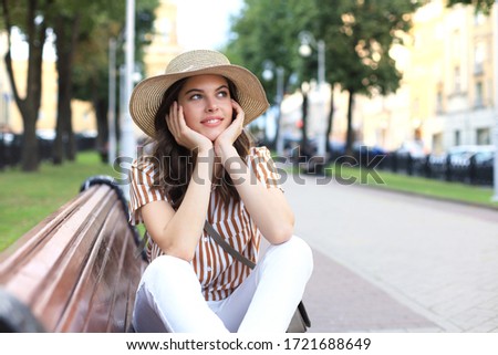 Beautiful smiling young brunette woman sitting on bench in park.