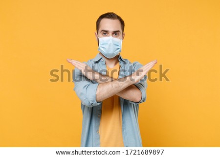 Young man in sterile face mask posing isolated on yellow background studio portrait. Epidemic pandemic coronavirus 2019-ncov sars covid-19 flu virus concept. Showing stop gesture with crossed hands