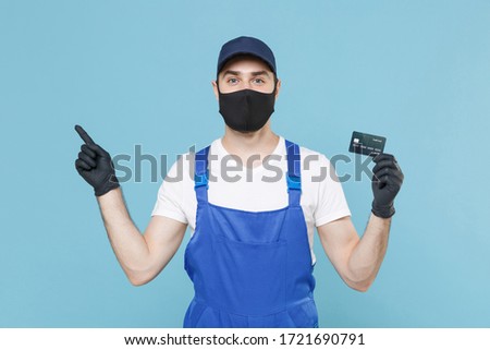 Delivery man in cap tshirt uniform sterile mask glove isolated on blue background studio Guy employee courier hold credit card Service quarantine pandemic coronavirus virus covid-19 2019-ncov concept