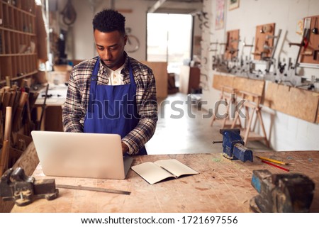 Male Craftsman In Carpentry Workshop For Bamboo Bicycles  Doing Accounts On Laptop Royalty-Free Stock Photo #1721697556