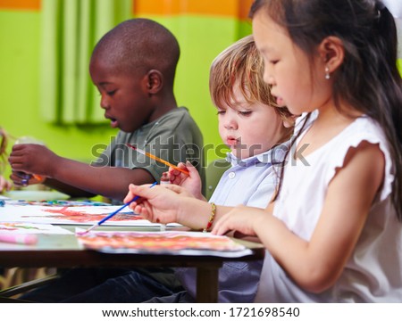 Different children concentrate together painting pictures in kindergarten