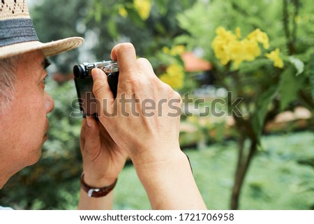 Close-up image of senior man taking photos of bloomig tree in his garden