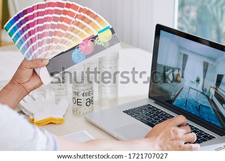 Interior designer looking at inspiring photos on laptop screen and choosing color for walls color from palette